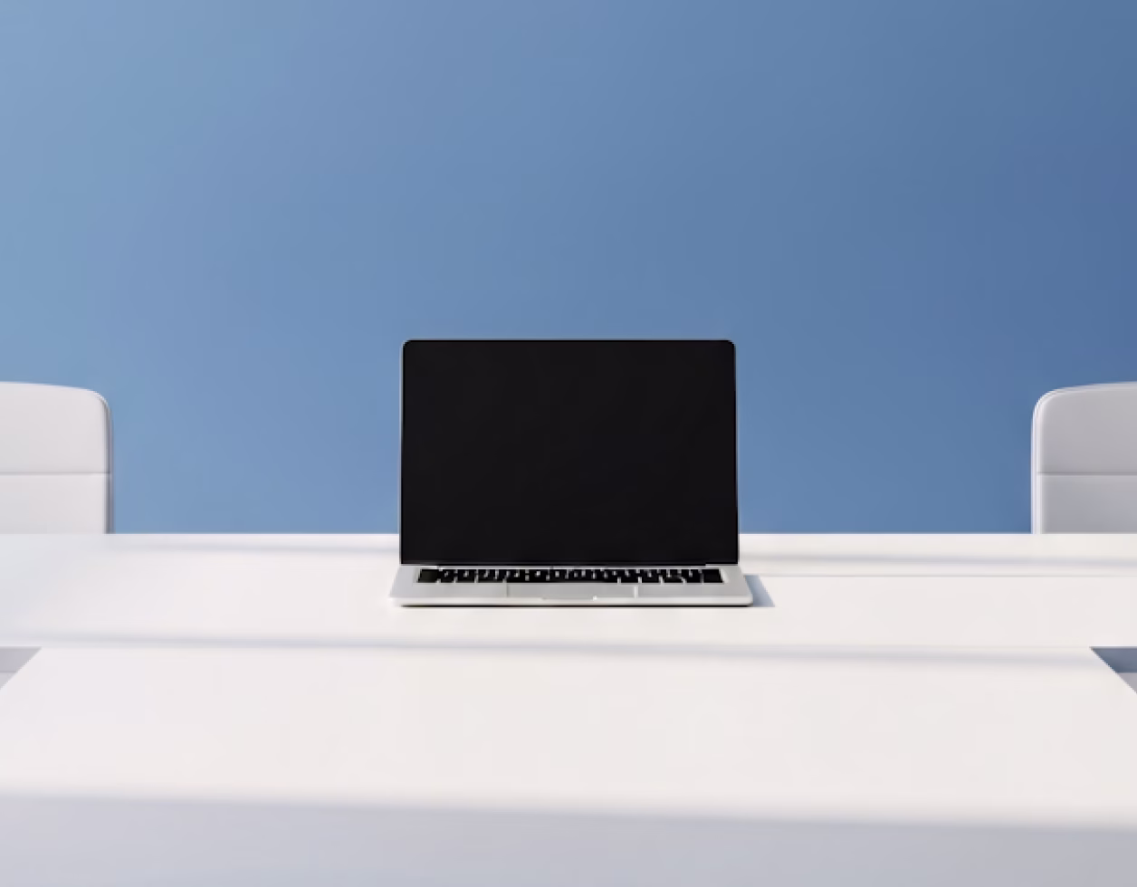 Closed laptop with a black screen on a white desk between two white chairs against a blue wall.